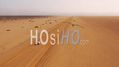 Aerial View Of A Safari Vehicle On A Dirt Road Heading Across A Flat Desert With Mist Or Fog In The Distance, Namibia - Video Drone Footage