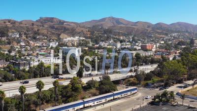 Aerial Video Drone Footage Of The Pacific Surfline Amtrak Train Passing Through The Southern California Beach Town Of Ventura, California With Freeway Foreground And Mountains Background
