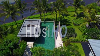 Aerial View Over A Woman Swimming In An Infinity Pool At Luxury Resort Of Elegant Home Complex Along The Coast Of Bali, Indonesia - Video Drone Footage