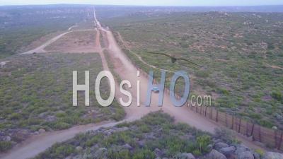 The American Flag Flies Over The U.S. Mexico Border Wall In The California Desert As A Border Patrol Passes Beneath - Video Drone Footage