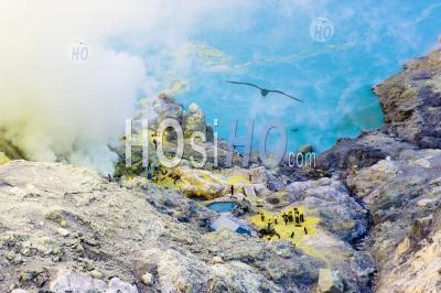 Birds Eye View Of Sulphur Miners Working By The Turquoise Acid Crater Lake At Kawah Ijen, Java, Indonesia
