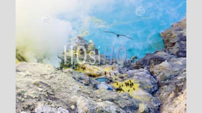 Birds Eye View Of Sulphur Miners Working By The Turquoise Acid Crater Lake At Kawah Ijen, Java, Indonesia