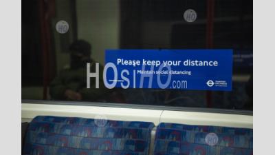 Person Wearing Face Mask On Public Transport, With Covid-19 Coronavirus Information Sign In London Underground Tube Train Carriage For Social Distancing In England, Uk