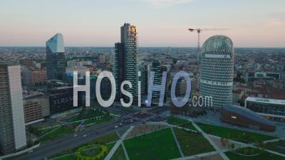 Aerial View Of Modern Design High Rise Office Buildings In Urban Borough At Twilight. Tilt Down On Traffic In Road Intersection. Milano, Italy. - Video Drone Footage