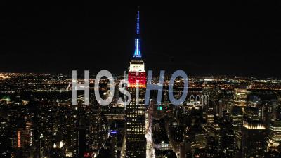 Good Aerial Of The Spire Of The Empire State Building Lit Up Red, White And Blue In New York City, New York - Video Drone Footage