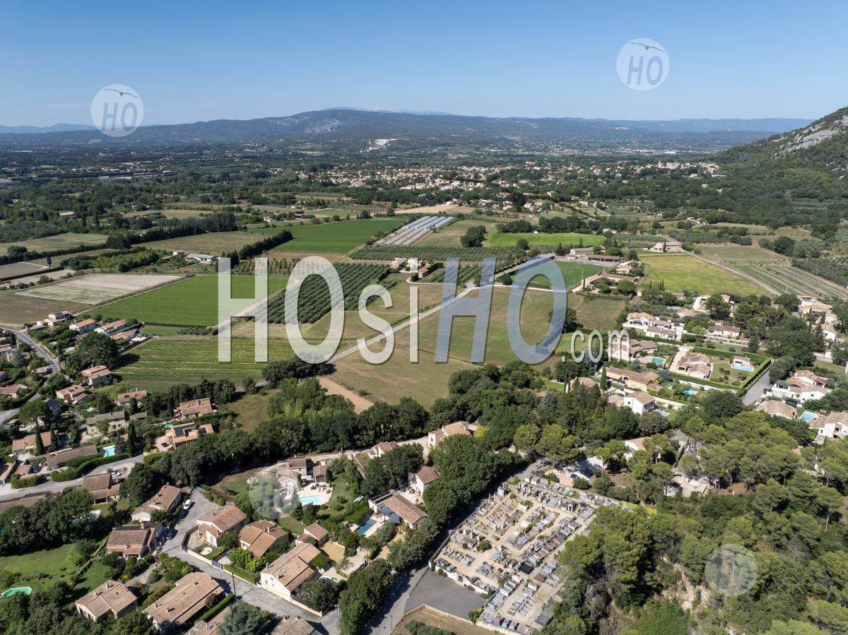 Taillades, Dans Le Vaucluse, Baigne Dans La Lumière Estivale De Midi, Offrant Un Paysage Où Forêts Verdoyantes Et Villages Pittoresques Nichés Sous Une Chaîne De Montagnes Rocheuses - Photographie Aérienne