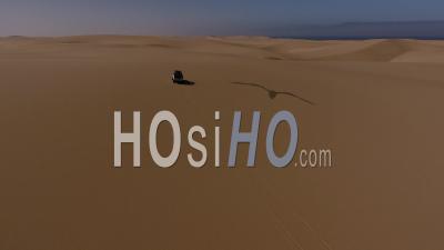 White Pick Up Driving Forward On Sand Dune In The Namib Desert, Atlantic Ocean On The Left, Followed By Drone
